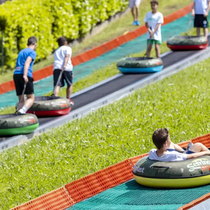 Kinder fahren auf einer Sommerrodelbahn in Reifen den Hügel hinunter.