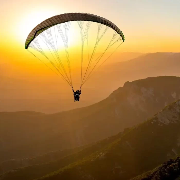 Eine Person gleitet mit einem Gleitschirm bei Sonnenuntergang über eine Berglandschaft.
