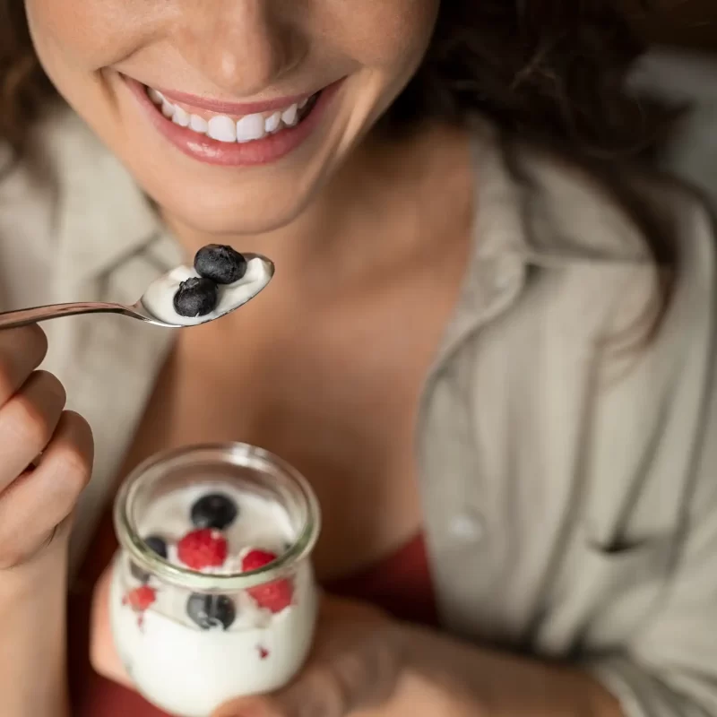 Donna sorridente mangia yogurt con frutti di bosco da un barattolo.